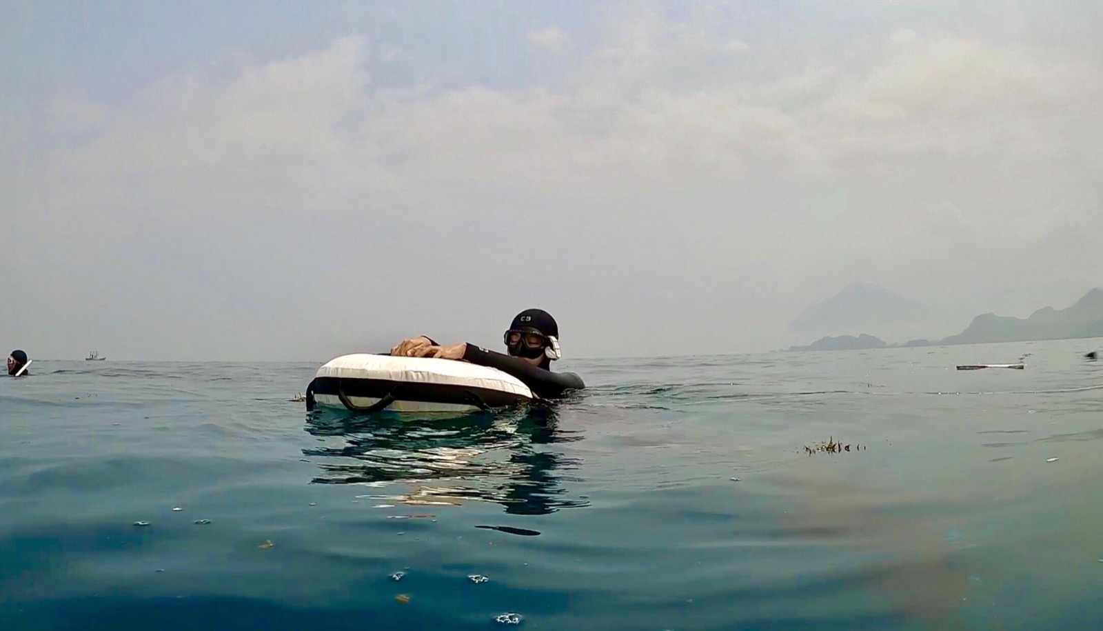 A freediver resting at the surface buoy, with distant islands